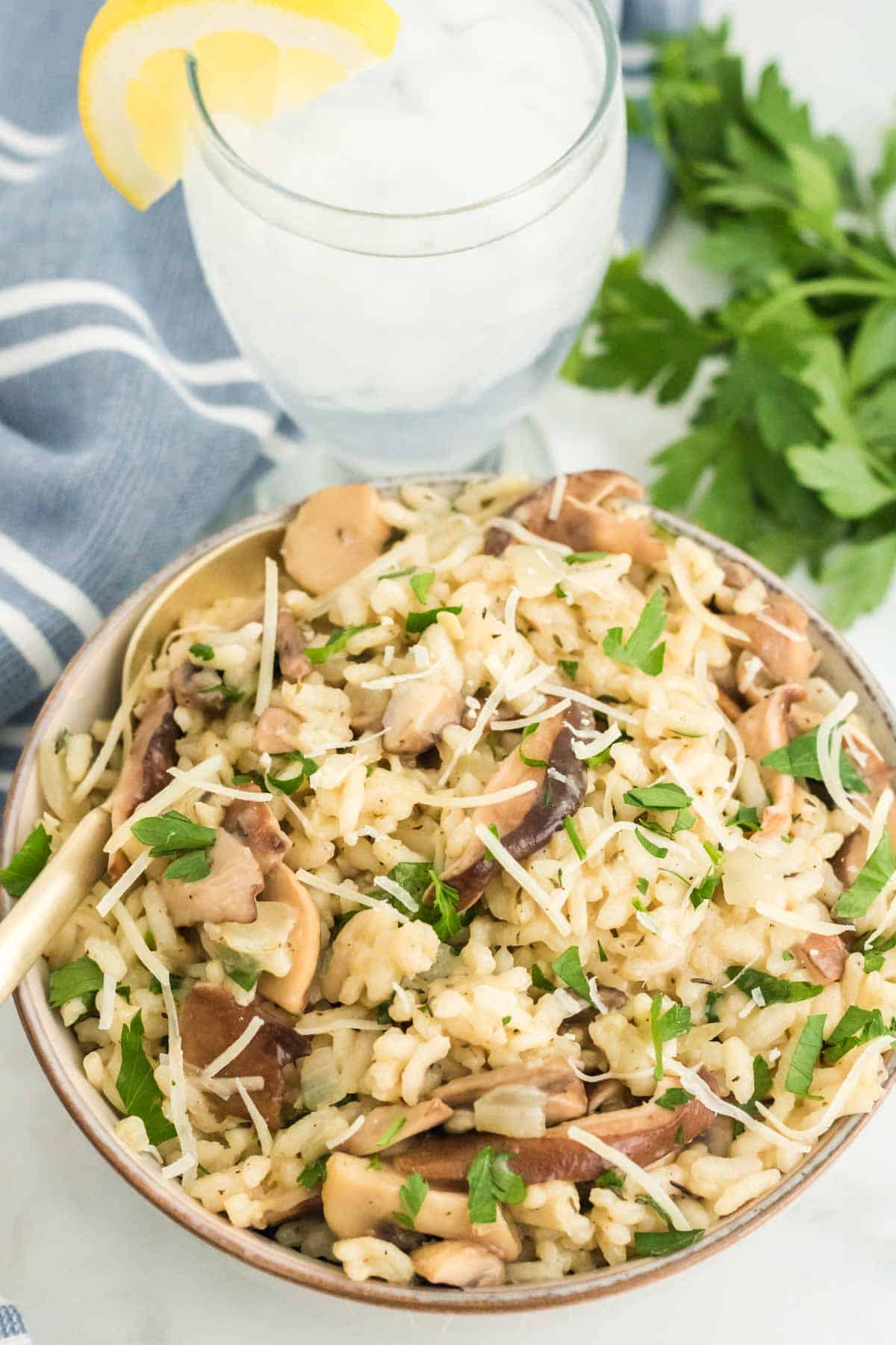 A bowl of mushroom risotto next to a glass of lemonade garnished with a lemon wedge.