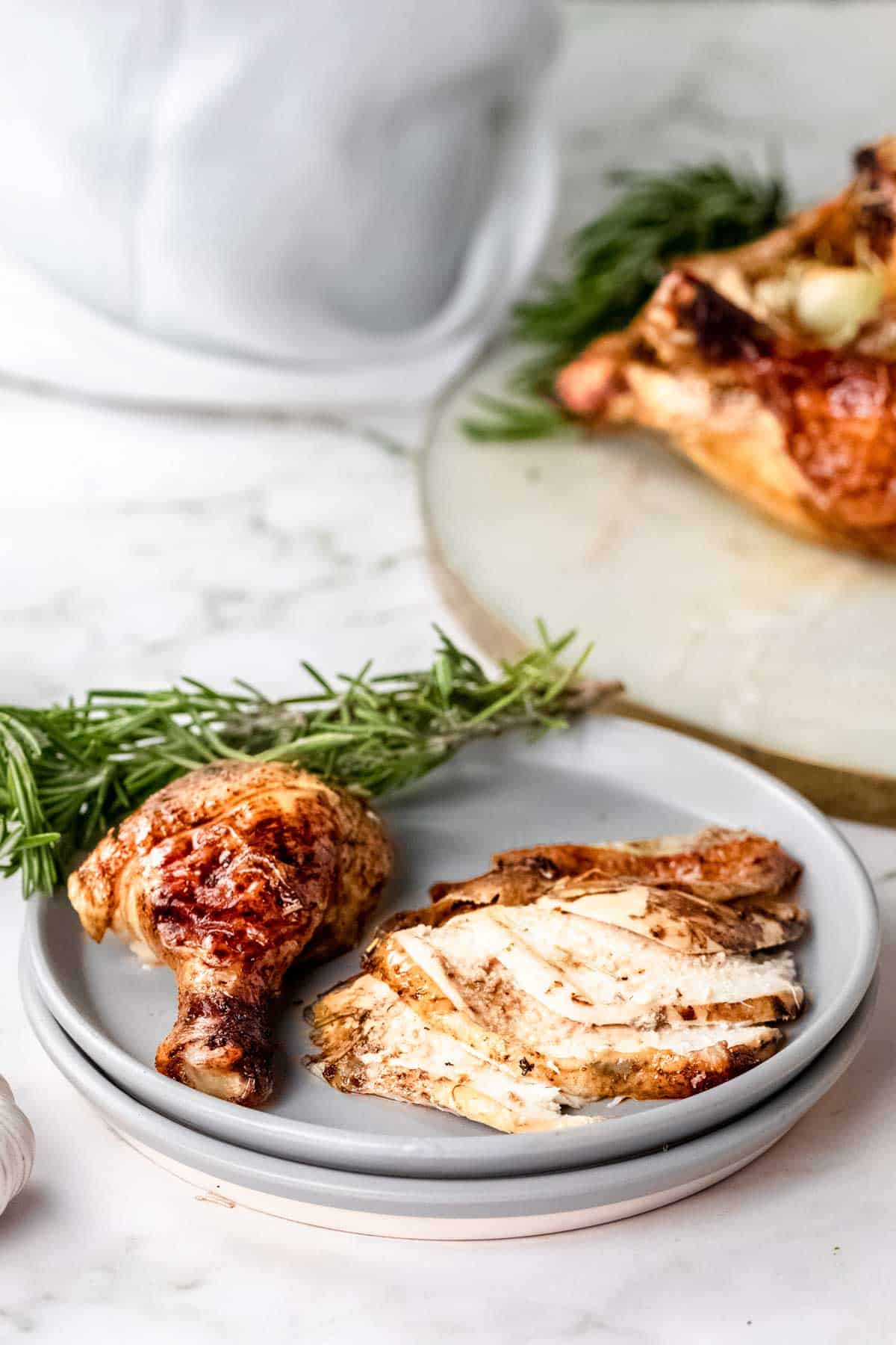 Carved rosemary balsamic roast chicken pieces on a plate next to fresh rosemary sprigs.