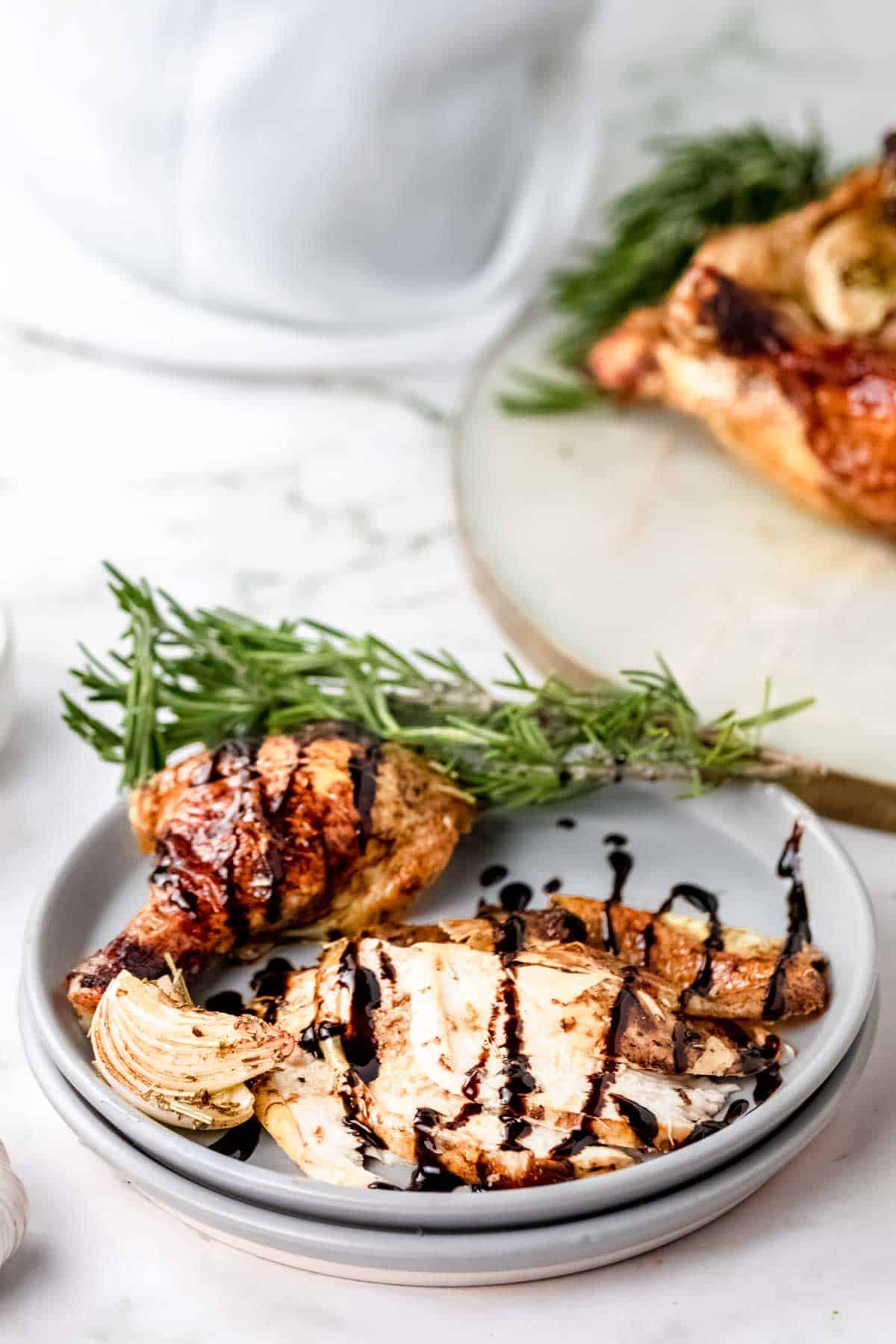 Carved rosemary balsamic roast chicken pieces on a plate drizzled with balsamic sauce, next to fresh rosemary sprigs.