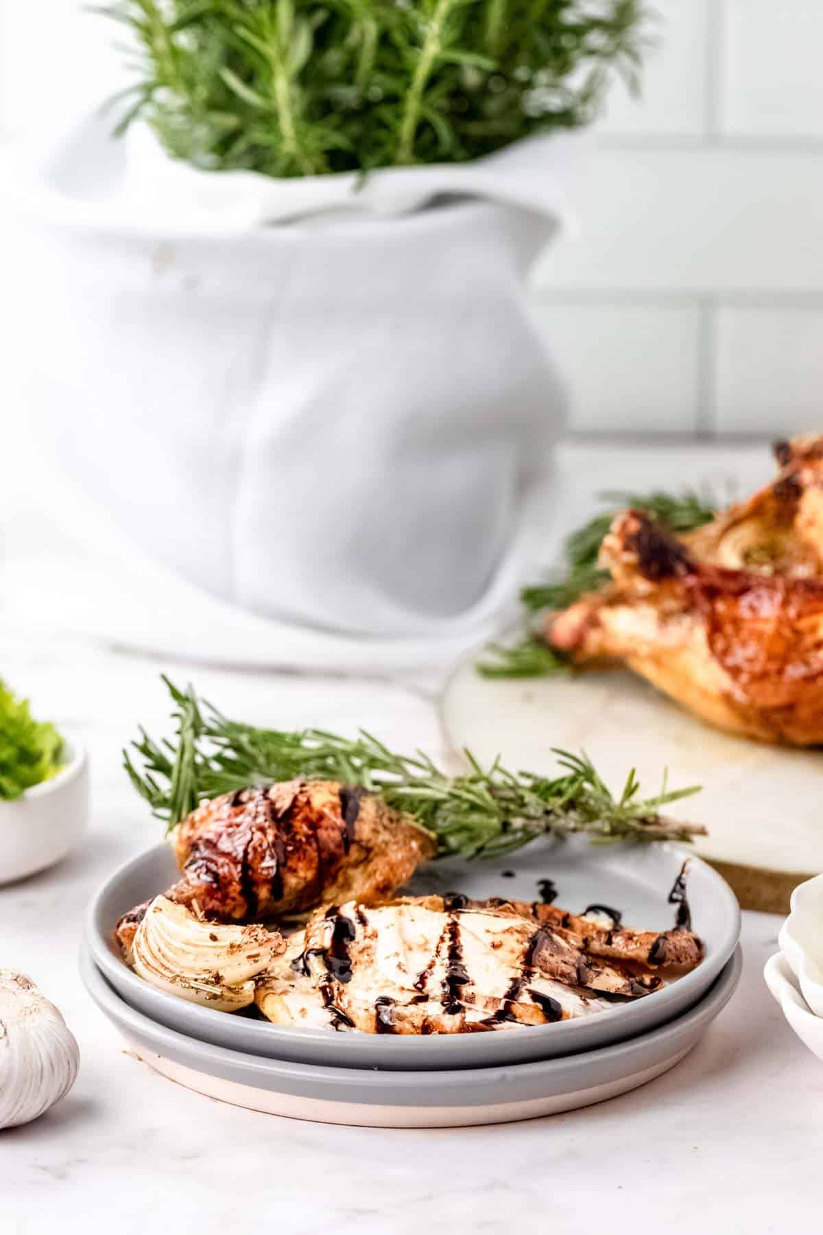 Carved rosemary balsamic roast chicken pieces on a plate drizzled with balsamic sauce, next to fresh rosemary sprigs.