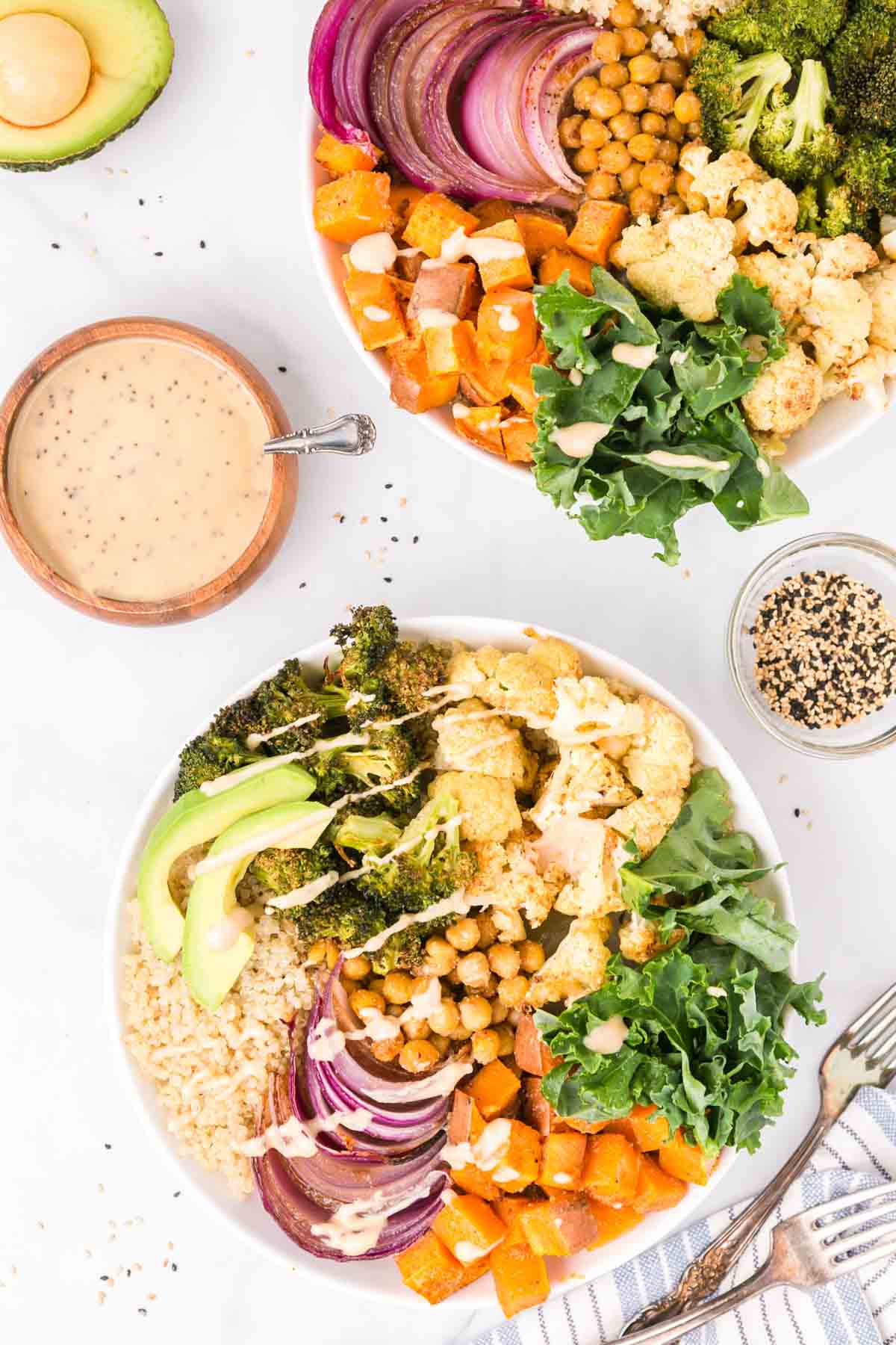 Overhead view of two sweet potato buddha bowls drizzled with dressing next to bowls of dressing and seeds.