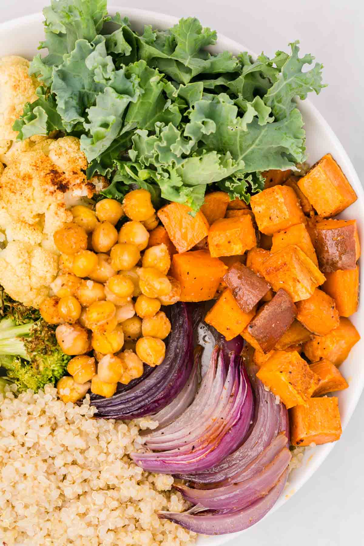 Close up overhead view of a sweet potato buddha bowl with roasted veggies, chickpeas, broccoli, kale, and quinoa.