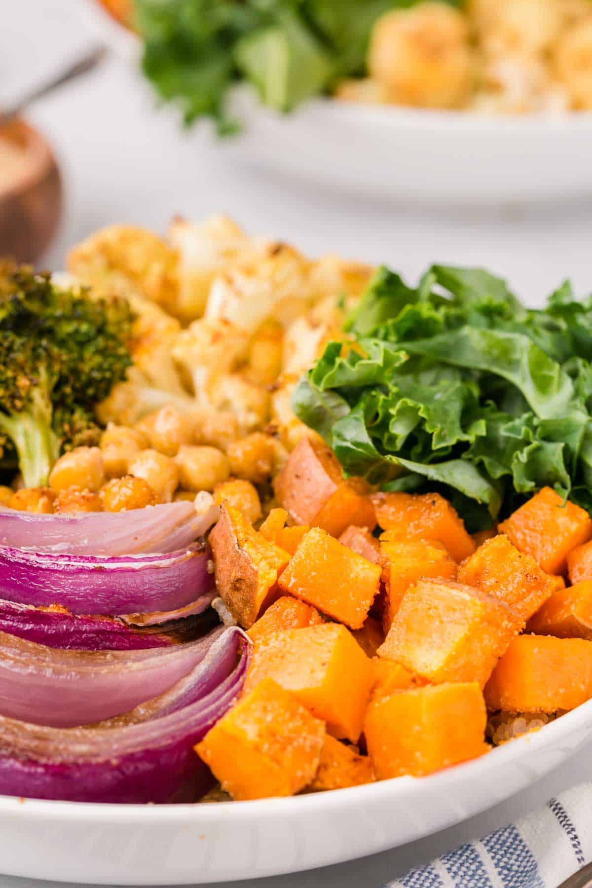 Close up of a sweet potato buddha bowl with roasted veggies, chickpeas, broccoli, kale, and quinoa.