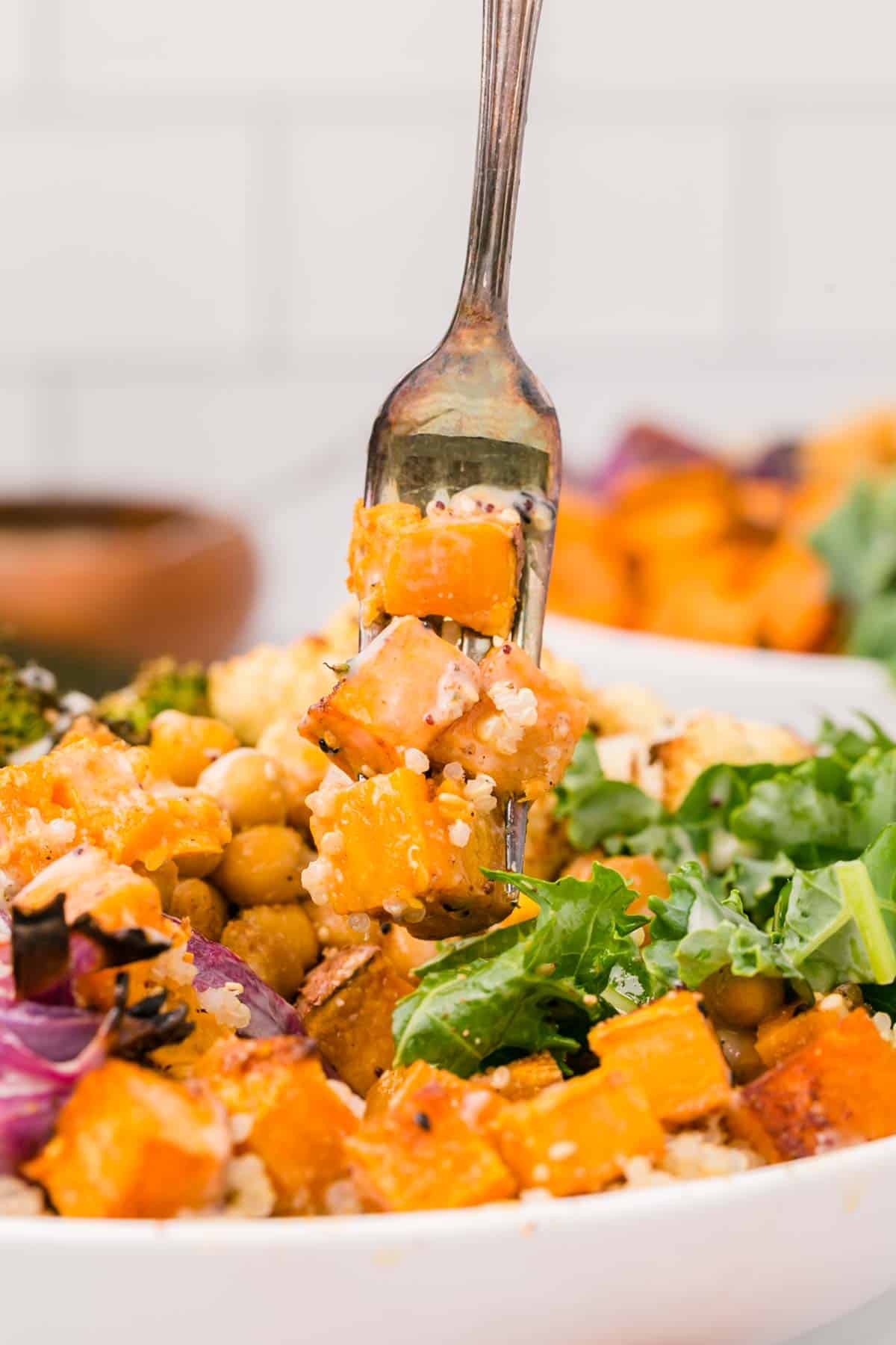 A forkful of roasted sweet potato held over a sweet potato buddha bowl.