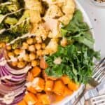 Close up overhead view of a sweet potato buddha bowl with roasted veggies, chickpeas, broccoli, kale, and quinoa, drizzled with dressing.