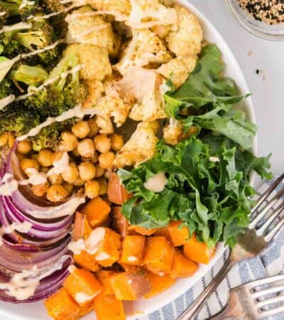 Close up overhead view of a sweet potato buddha bowl with roasted veggies, chickpeas, broccoli, kale, and quinoa, drizzled with dressing.