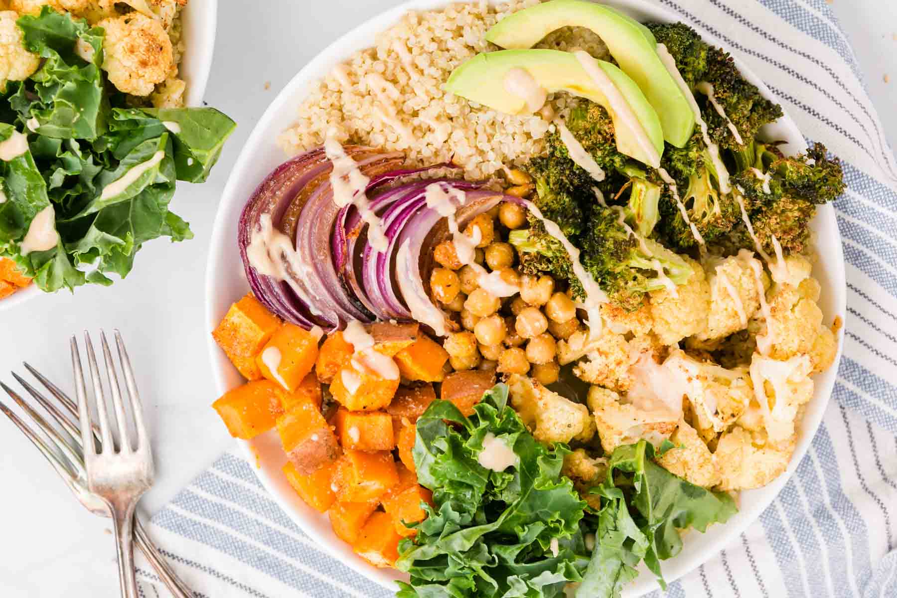 Overhead view of a sweet potato buddha bowl with roasted veggies, chickpeas, broccoli, kale, and quinoa, drizzled with dressing.