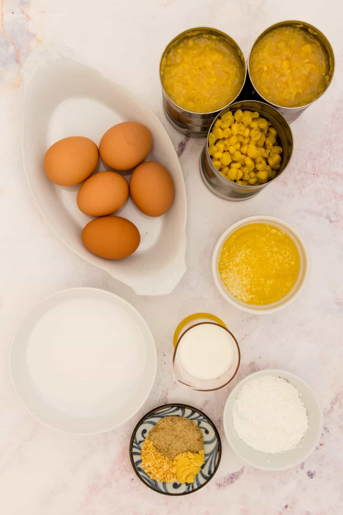 Corn pudding ingredients in bowls and containers on a marble countertop.