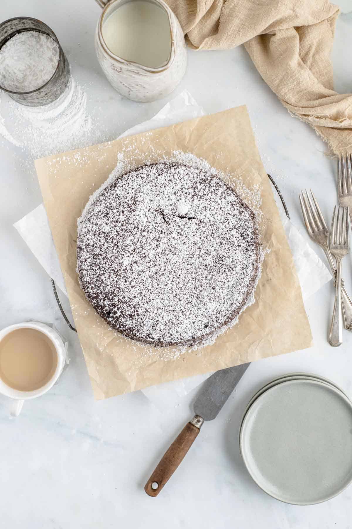 Overhead view of a flourless chocolate torte on a sheet of parchment paper, surrounded by baking supplies.