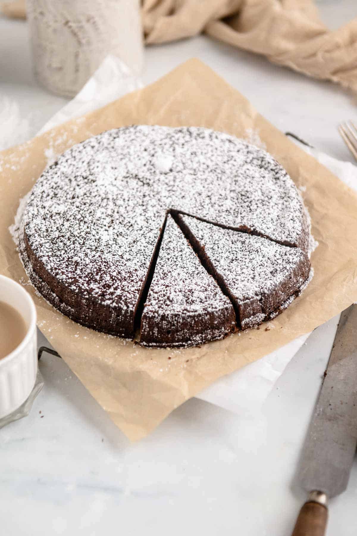 Overhead view of a flourless chocolate torte dusted with powdered sugar, with two slices cut out.