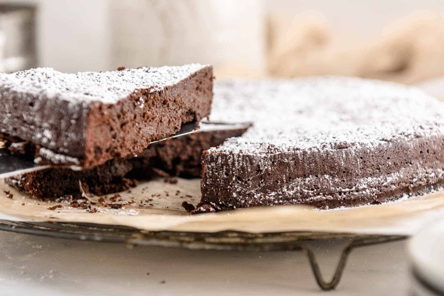 A slice is lifted from a flourless chocolate torte on a parchment-lined wire cooling rack.