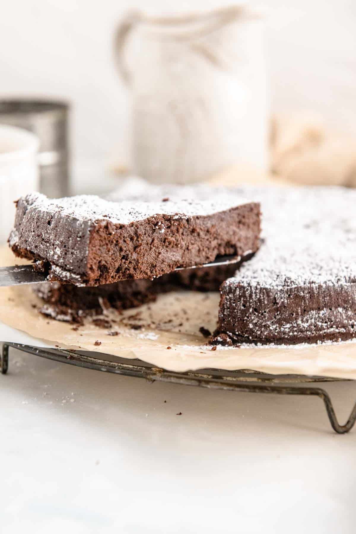 A slice is lifted from a flourless chocolate torte on a parchment-lined wire cooling rack.