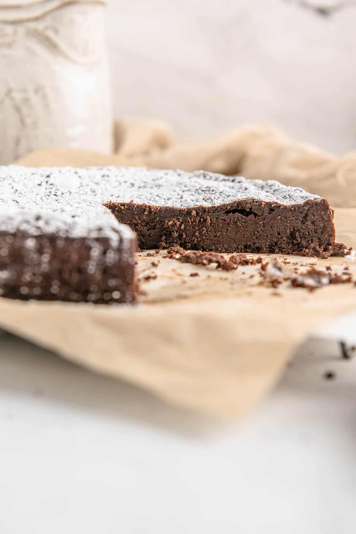 Flourless chocolate torte on a sheet of parchment paper with slices missing.