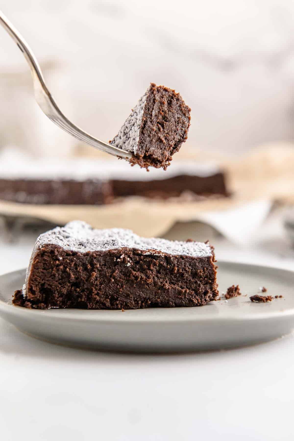 A forkful of chocolate torte held above a slice on a plate.