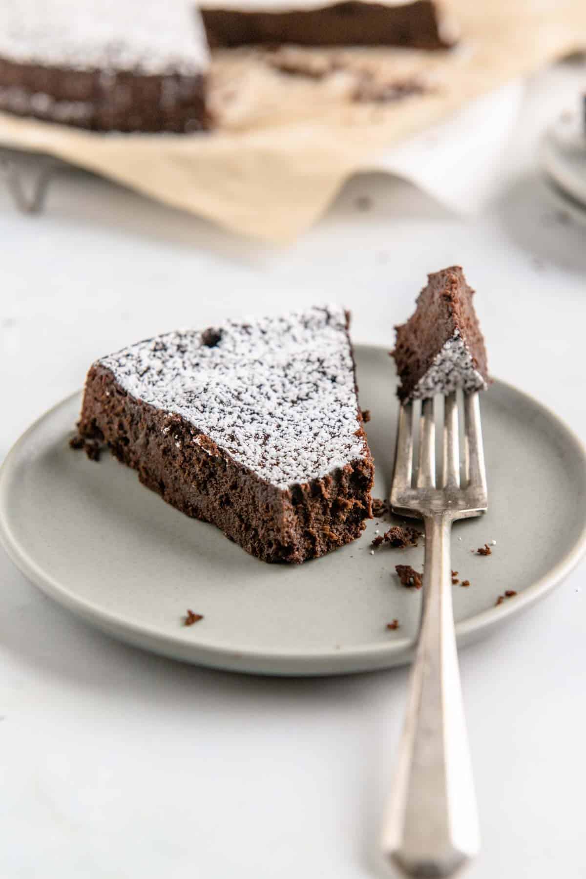 A forkful of chocolate torte next to a slice on a grey plate.