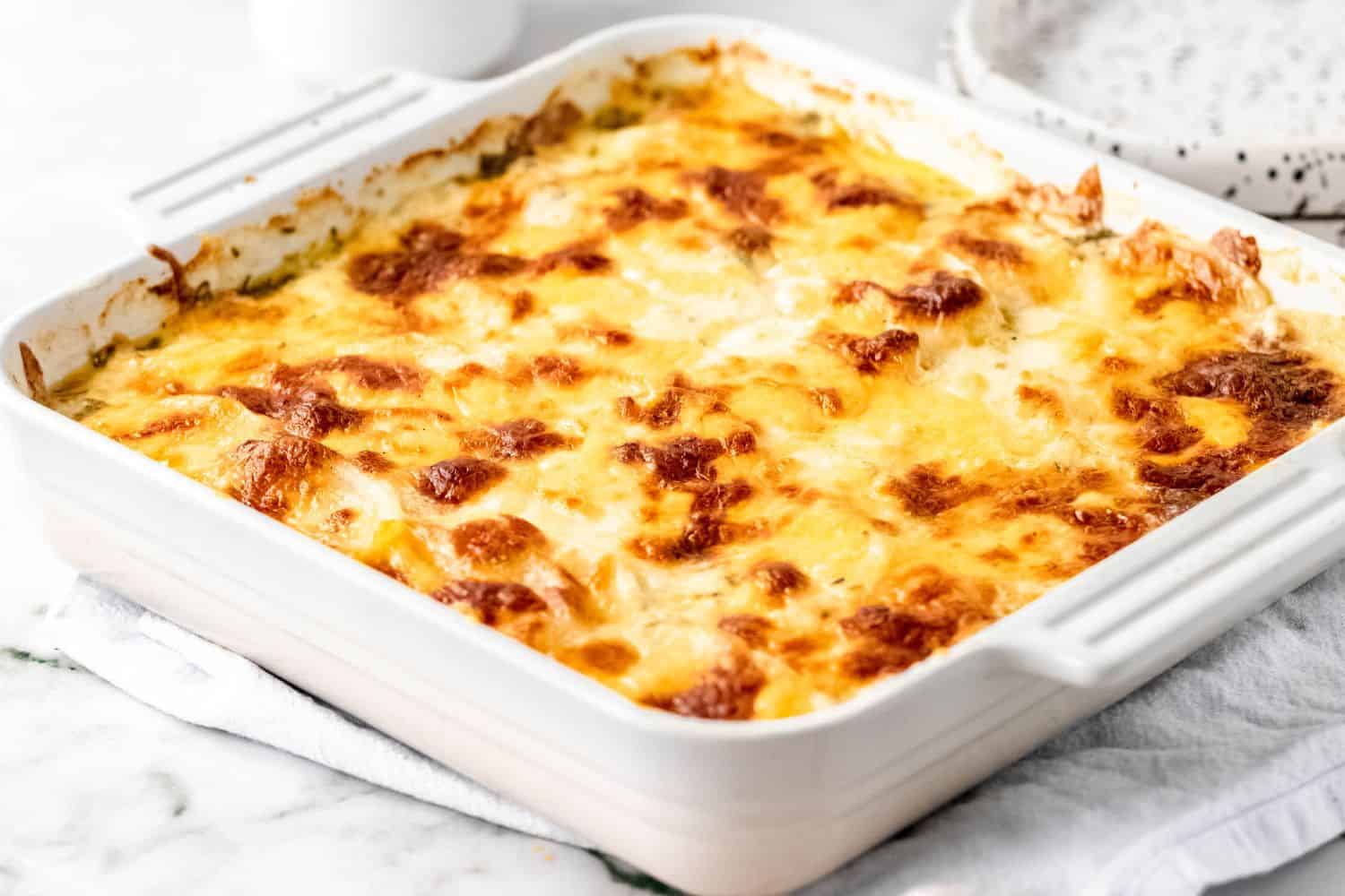 A square casserole dish filled with cheesy scalloped potatoes set on a dish towel to cool.