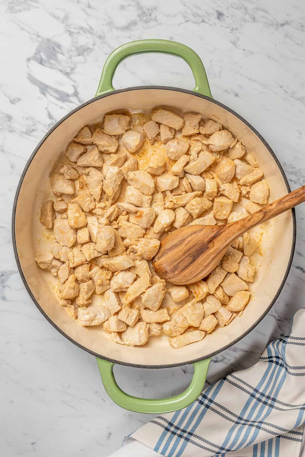 Cooked cubed chicken inside a large pot with a wooden spoon.