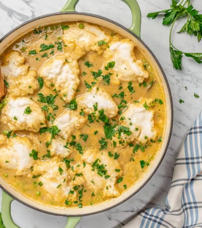 Overhead view of gluten-free chicken and dumpling soup inside a large pot, garnished with fresh chopped parsley.