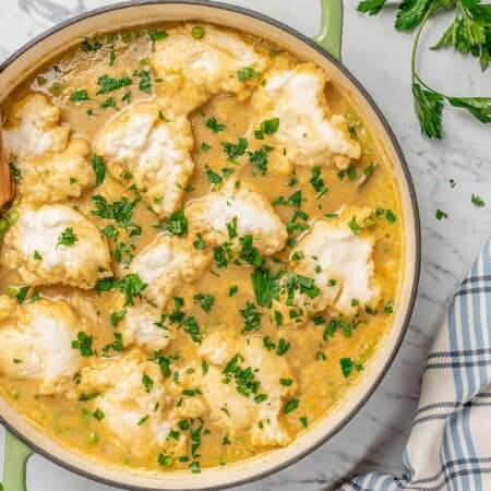 Overhead view of gluten-free chicken and dumpling soup inside a large pot, garnished with fresh chopped parsley.