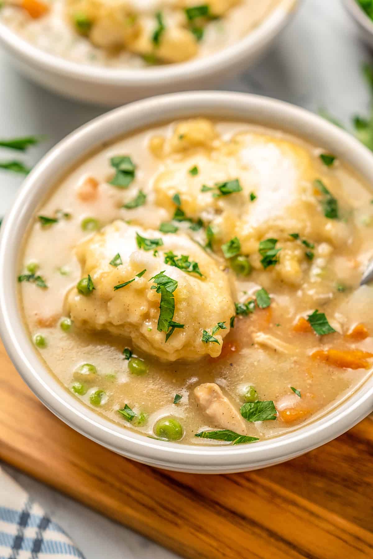 A bowl of gluten-free chicken and dumpling soup on a wooden board.