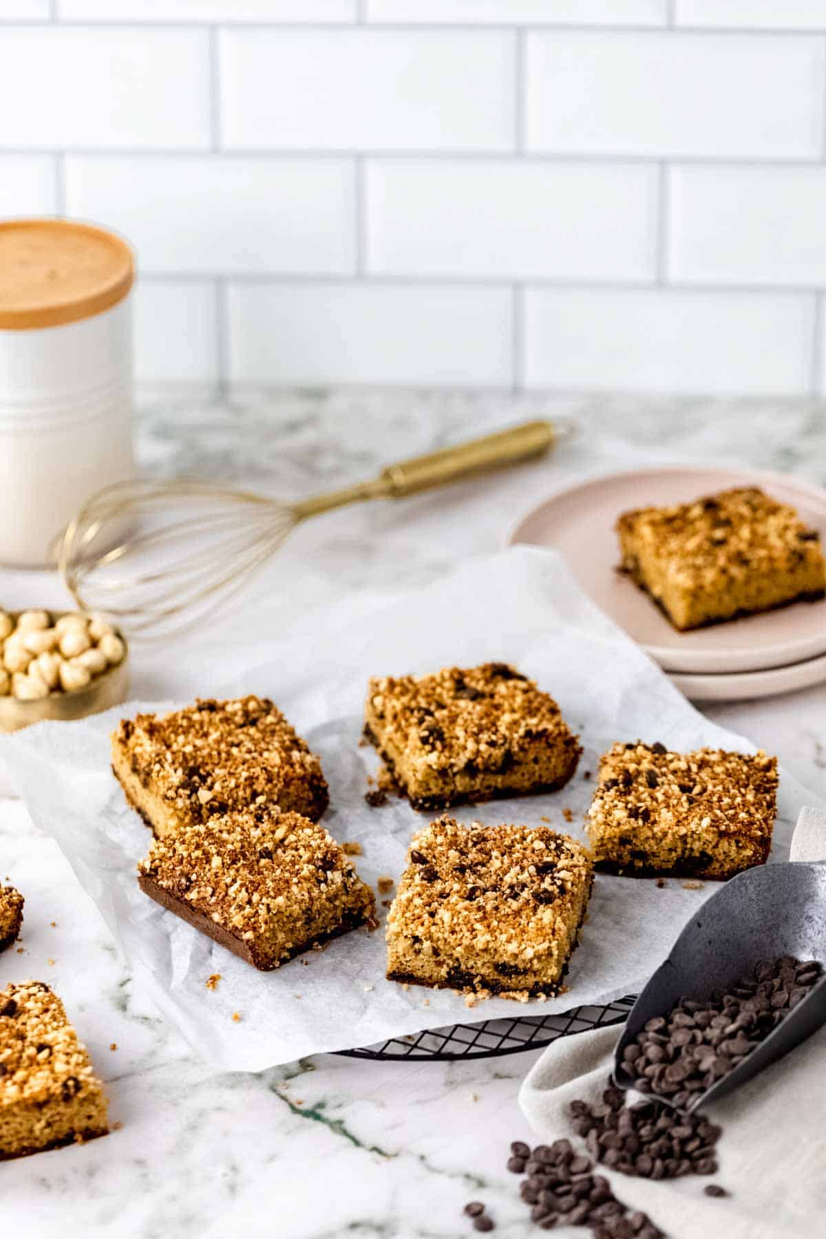 Squares of chocolate hazelnut crumb cake on a paper-lined plate, on a white marble countertop.