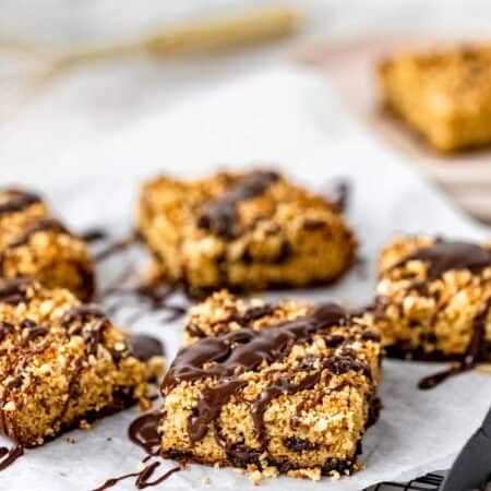 Squares of chocolate hazelnut crumb cake drizzled with chocolate glaze on a paper-lined plate.