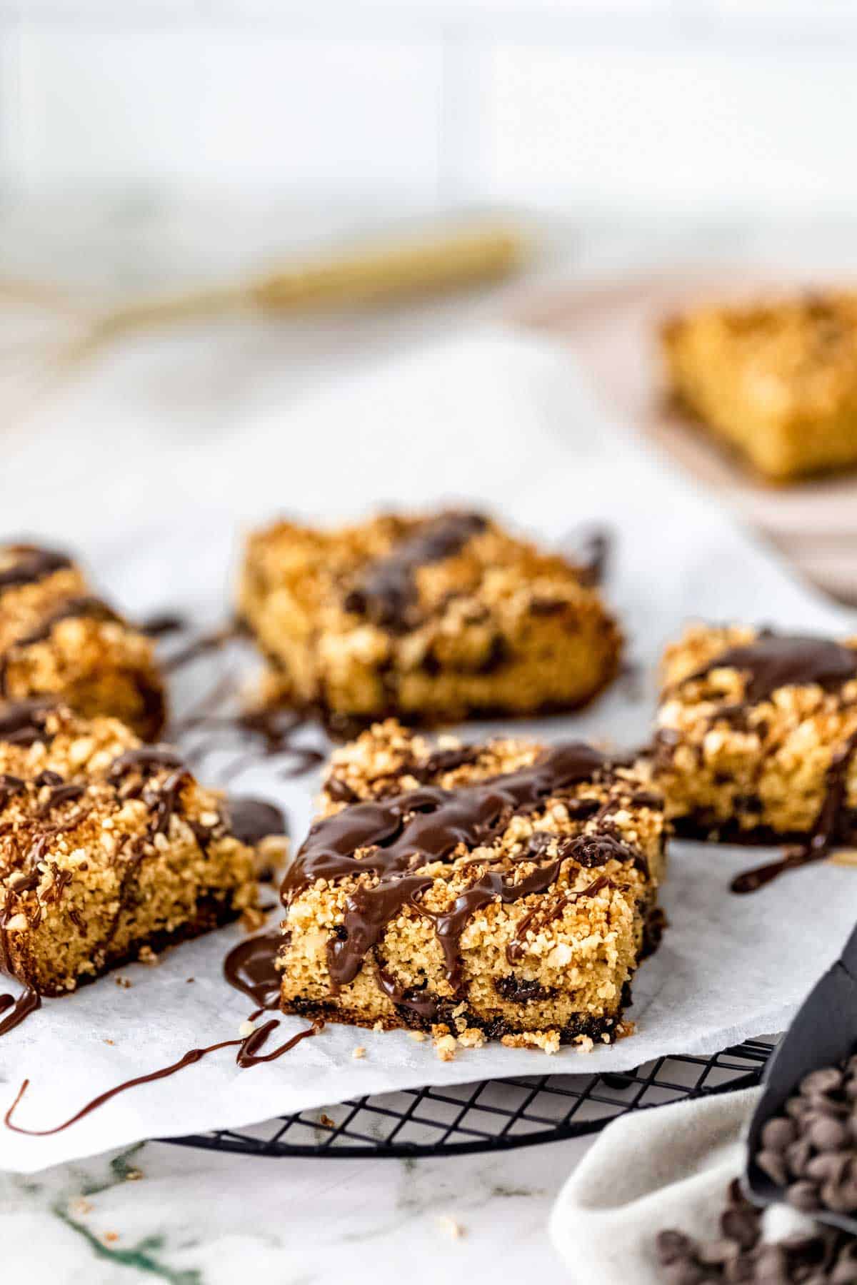 Squares of chocolate hazelnut crumb cake drizzled with chocolate glaze on a paper-lined plate.