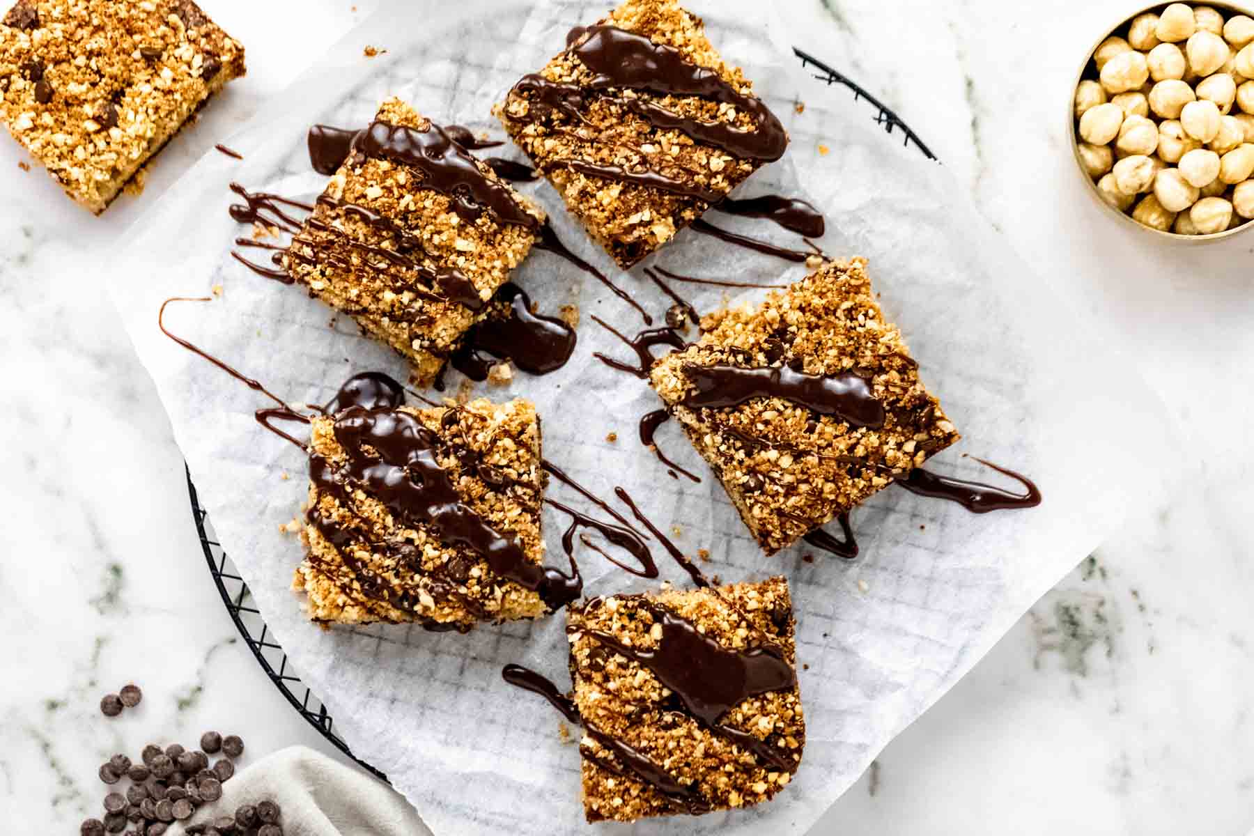 Overhead view of squares of chocolate hazelnut crumb cake drizzled with chocolate glaze on a paper-lined plate.