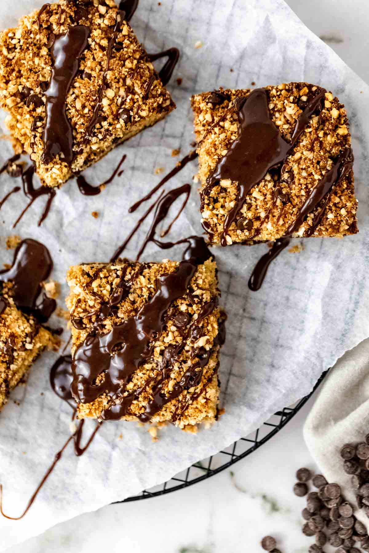 Close up overhead view of squares of chocolate hazelnut crumb cake drizzled with chocolate glaze on a paper-lined plate.