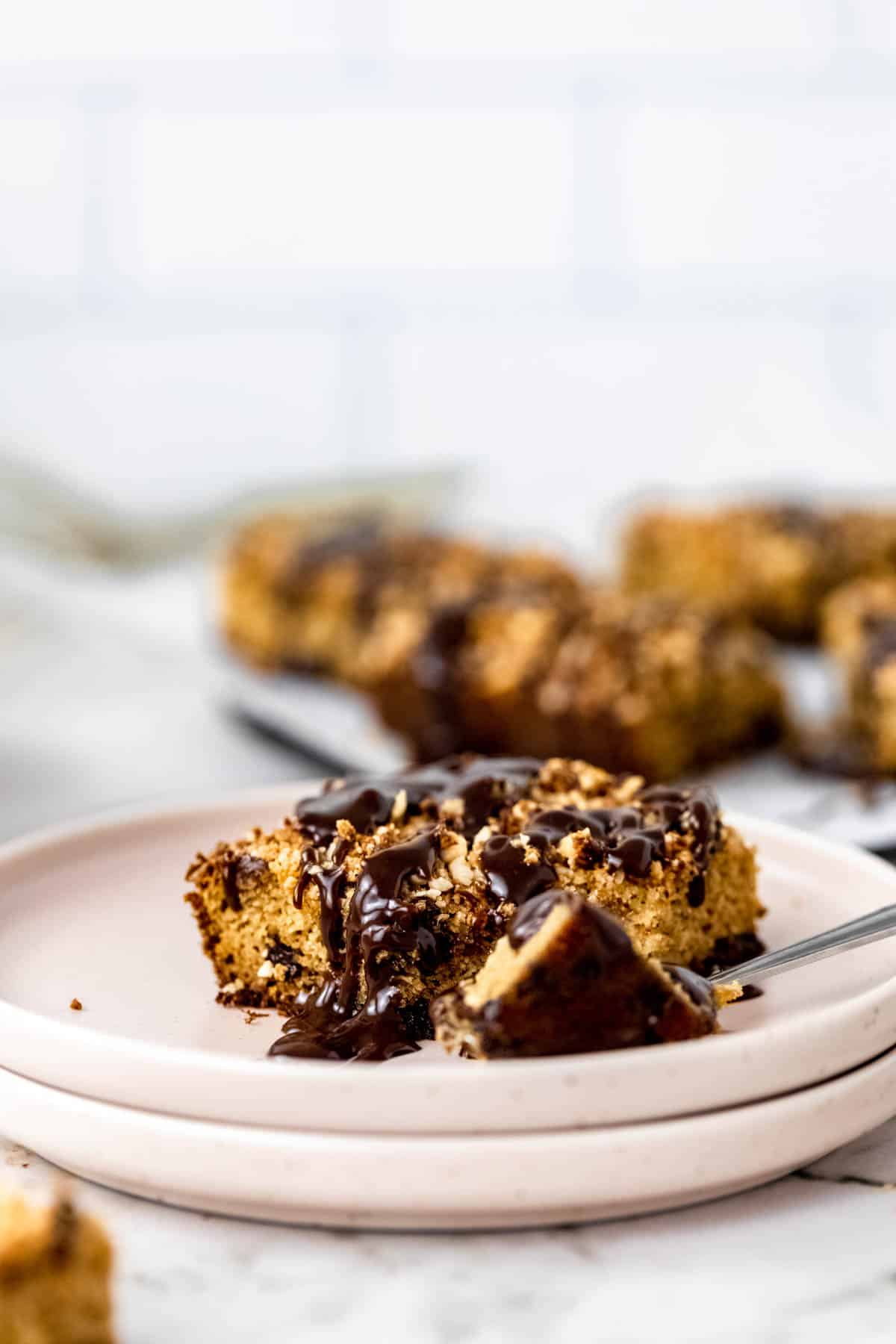 A slice of gluten-free chocolate hazelnut crumb cake on a plate, drizzled with chocolate glaze next to a fork.