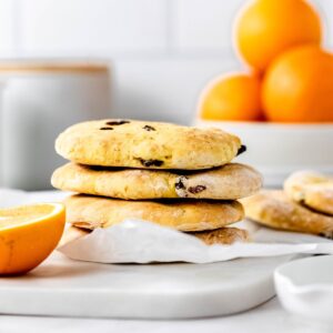 A stack of four gluten free cranberry orange pita breads on top of a piece of parchment paper on a marble cutting board with a bowl of oranges in the background.