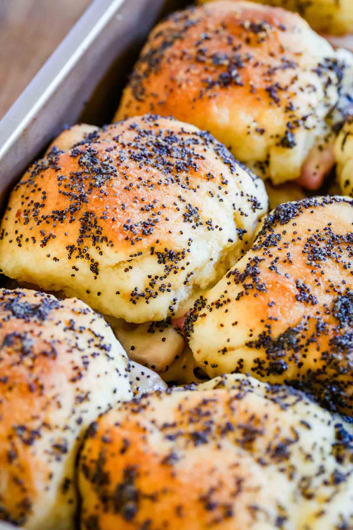 Gluten-free ham and cheese sliders in a baking pan topped with poppy seeds.