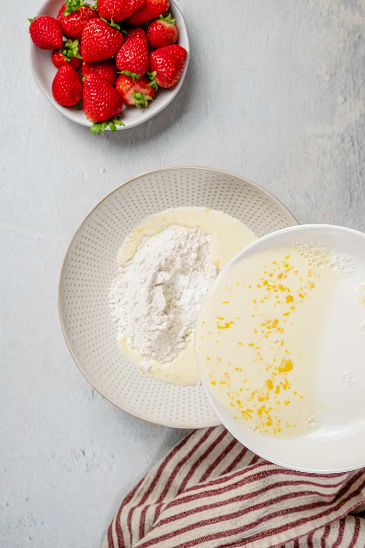 Adding wet ingredients to a mixing bowl of dry batter ingredients.