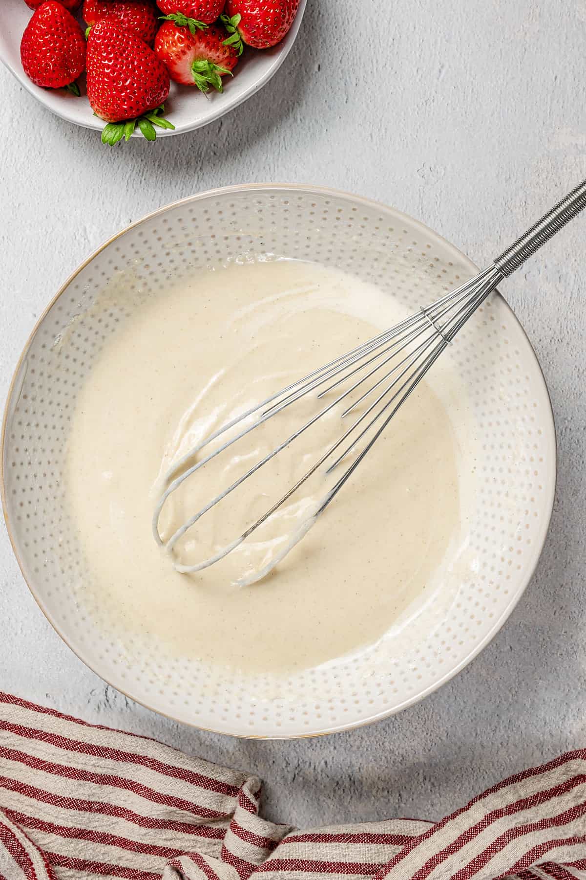 Gluten-free pikelet batter in a white mixing bowl with a whisk.