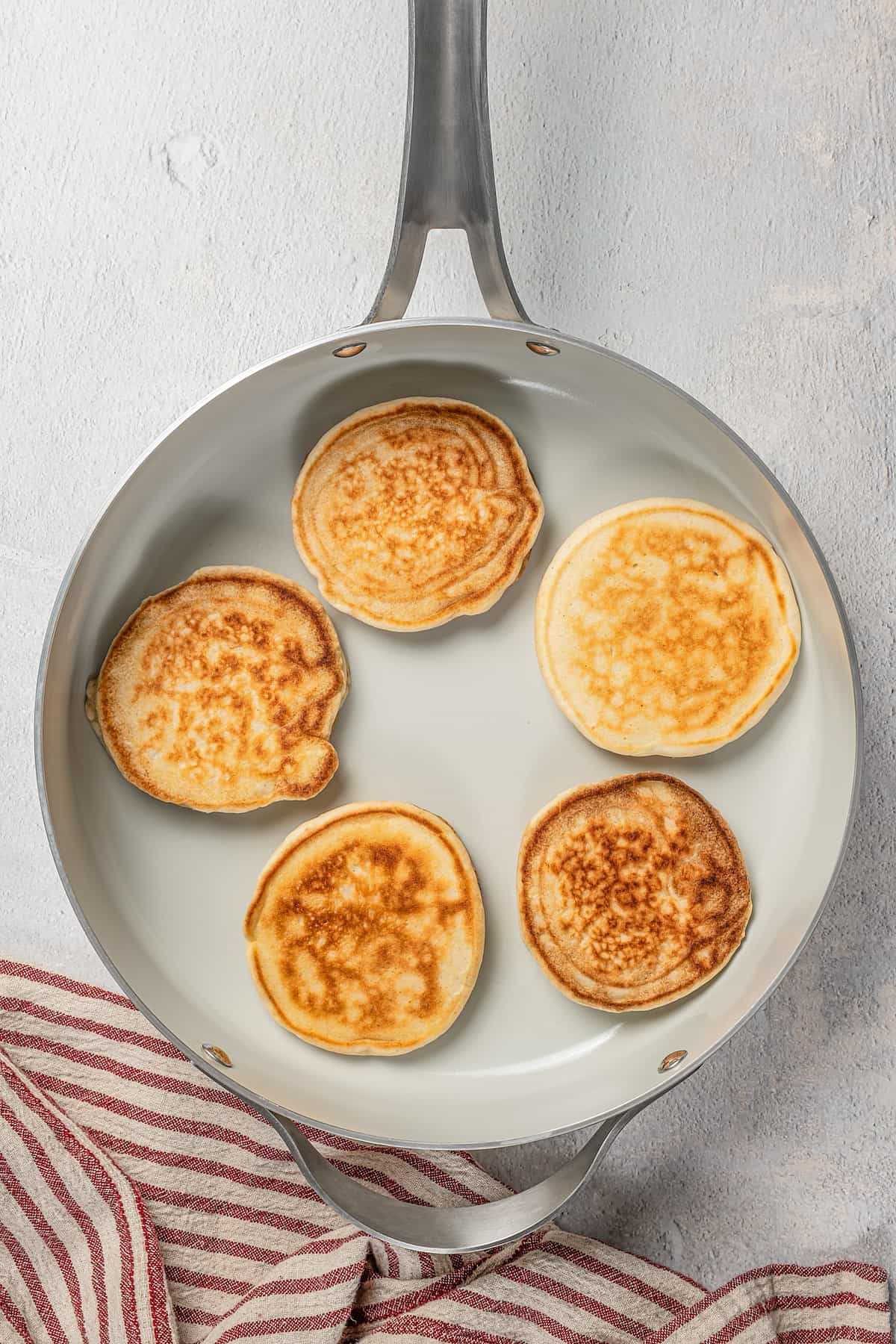 A batch of gluten-free pikelets cooking in a skillet.