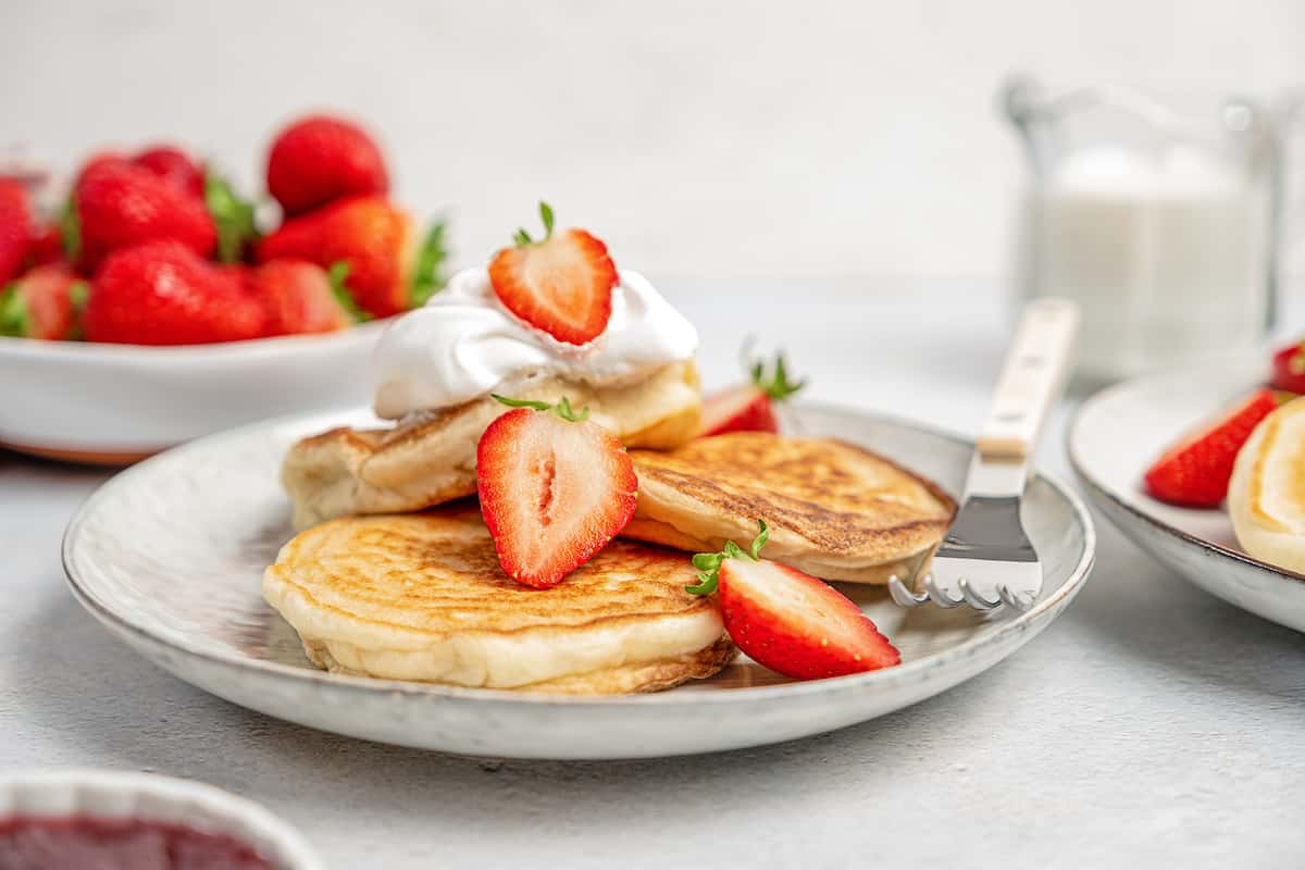 A plate of gluten-free pikelets topped with a dollop of whipped cream and sliced strawberries.