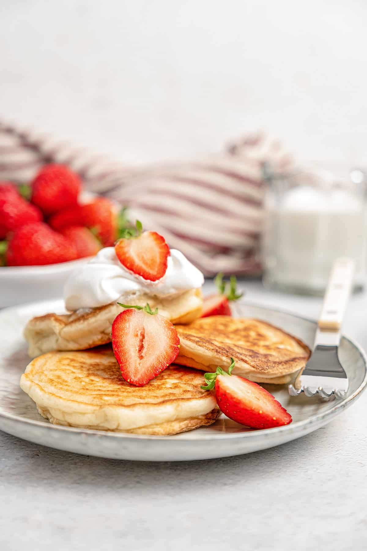 A plate of gluten-free pikelets topped with a dollop of whipped cream and sliced strawberries.