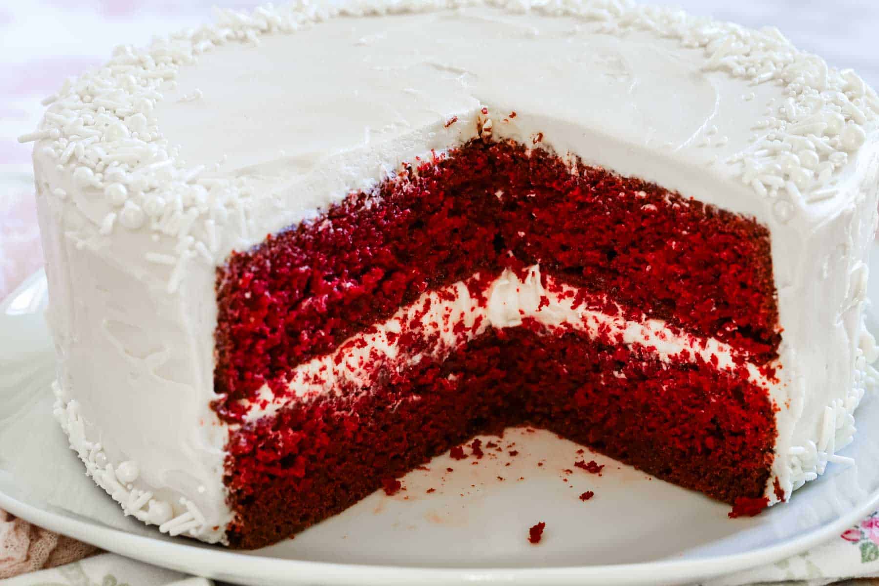 A two-layer gluten-free red velvet cake frosted with cream cheese frosting, with a large slice missing.