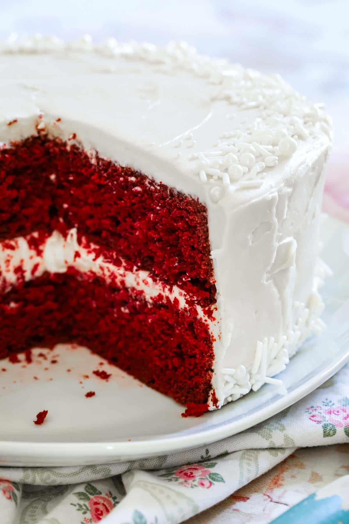 A two-layer gluten-free red velvet cake frosted with cream cheese frosting, with a large slice missing.