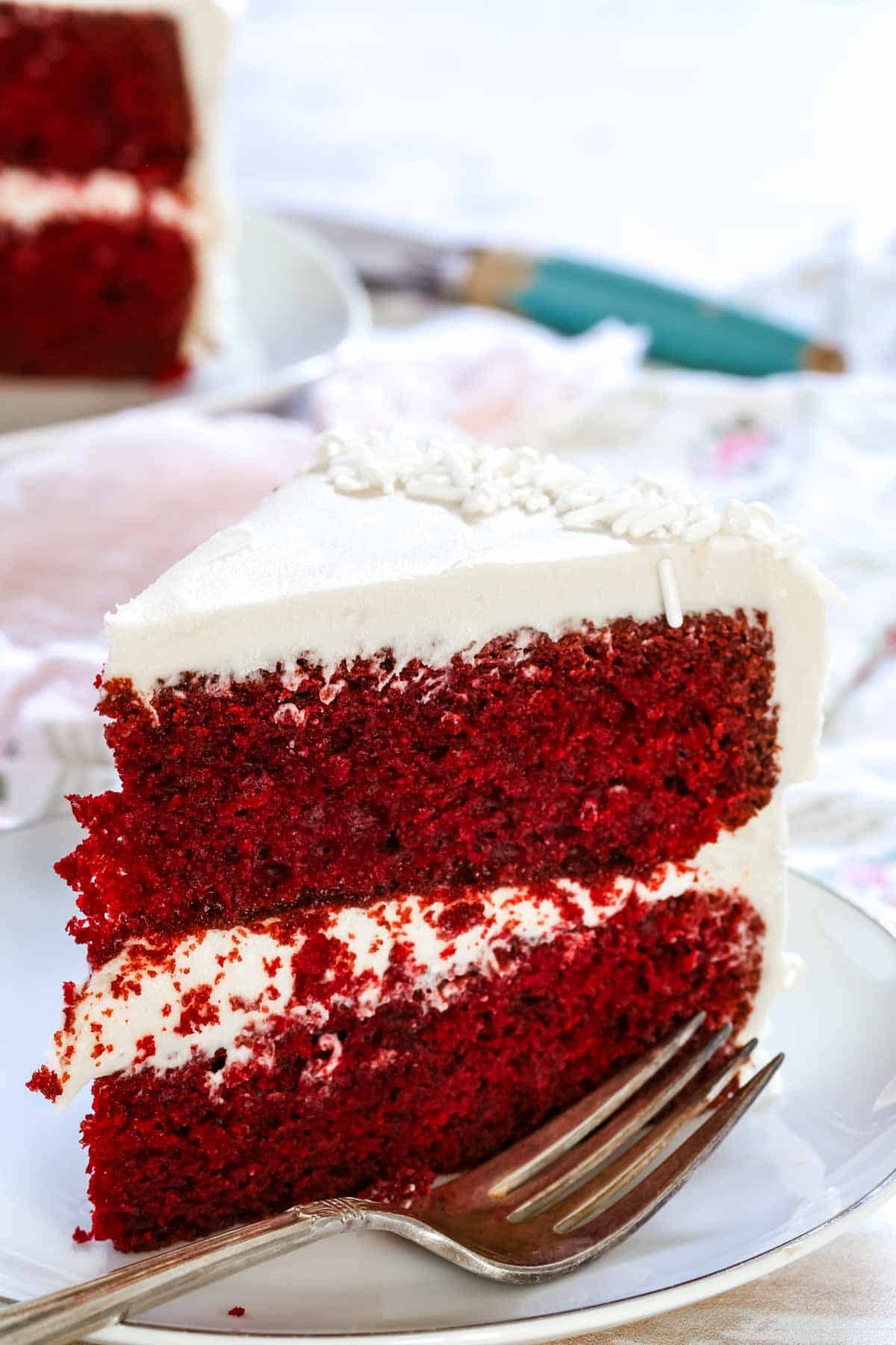 A slice of gluten-free red velvet cake on a white plate next to a fork.