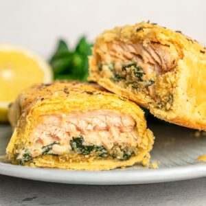 A golden-brown salmon wellington cut in half with one half propped up on the other on a plate.