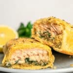 Two pieces of salmon en croute cut in half to show the interior on a plate with a lemon wedge, with text that says "Gluten Free Salmon Wellington".