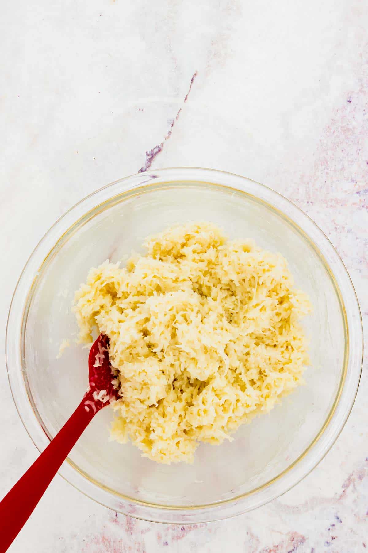 A red spatula in a glass bowl of a mixture of shredded coconut and sweetened condensed milk.