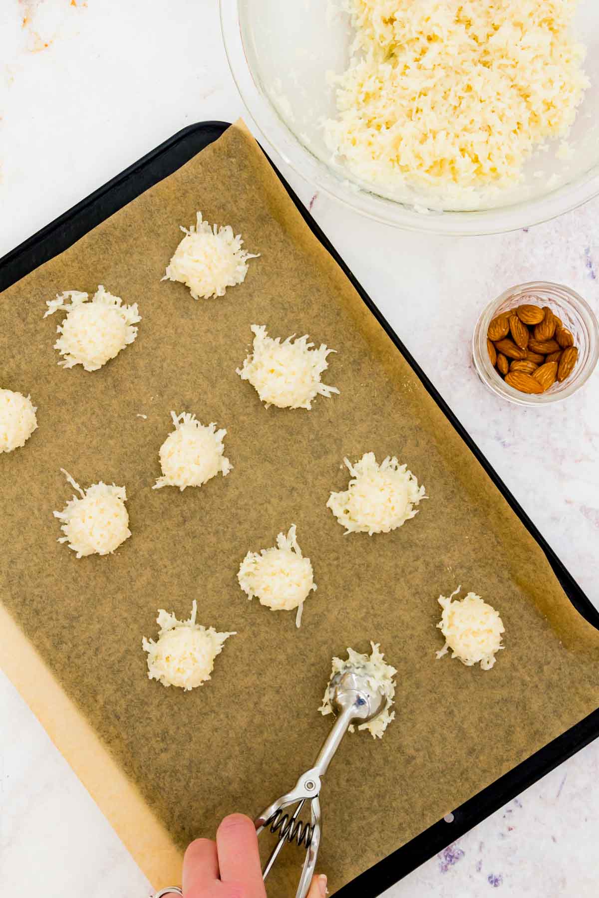 The coconut cookie mixture being scooped onto a parchment lined baking sheet.