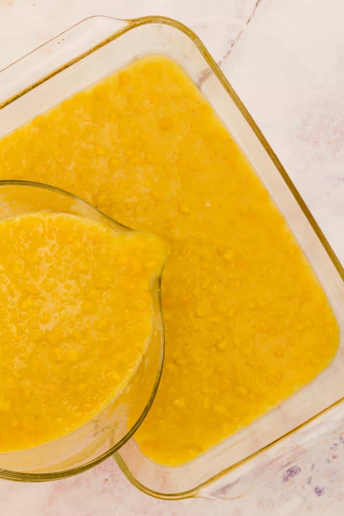 Corn pudding mixture being poured into a glass baking dish.