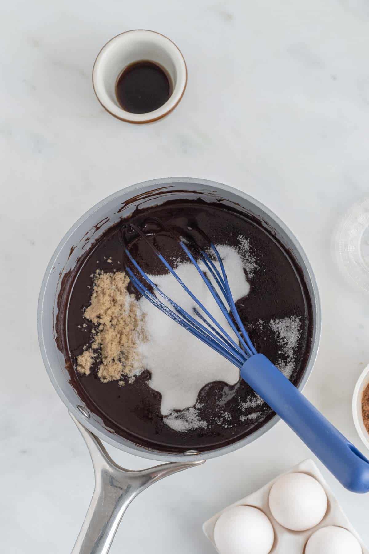 Sugar added to a mixing bowl with melted dark chocolate, with a whisk.