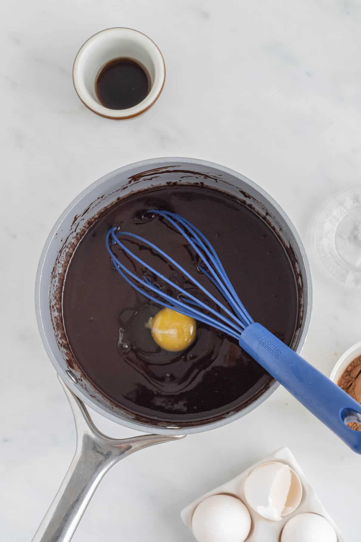 An egg added to the chocolate batter in a mixing bowl with a whisk.