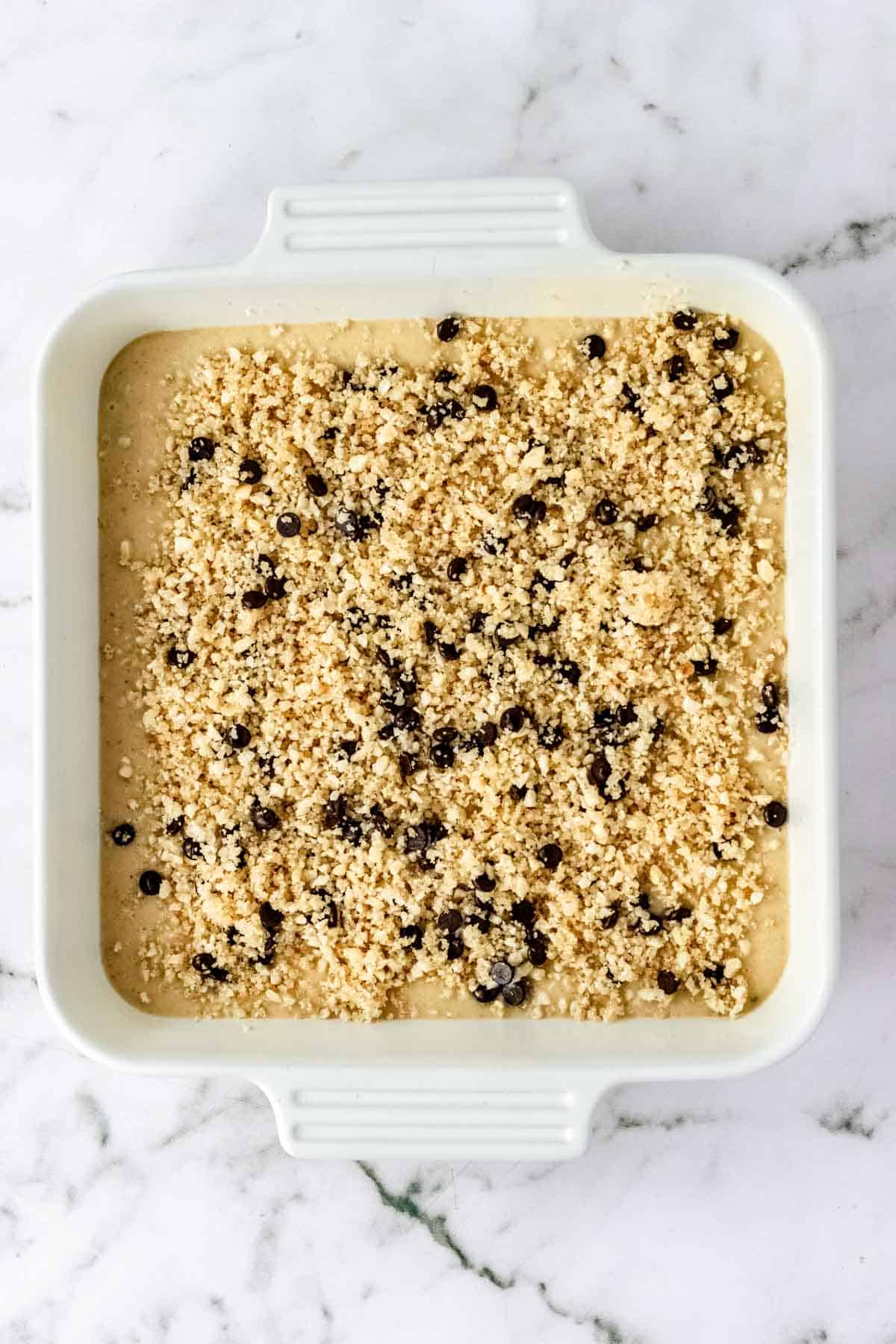 Hazelnut crumb topping sprinkled over top crumb cake batter in a ceramic baking dish.