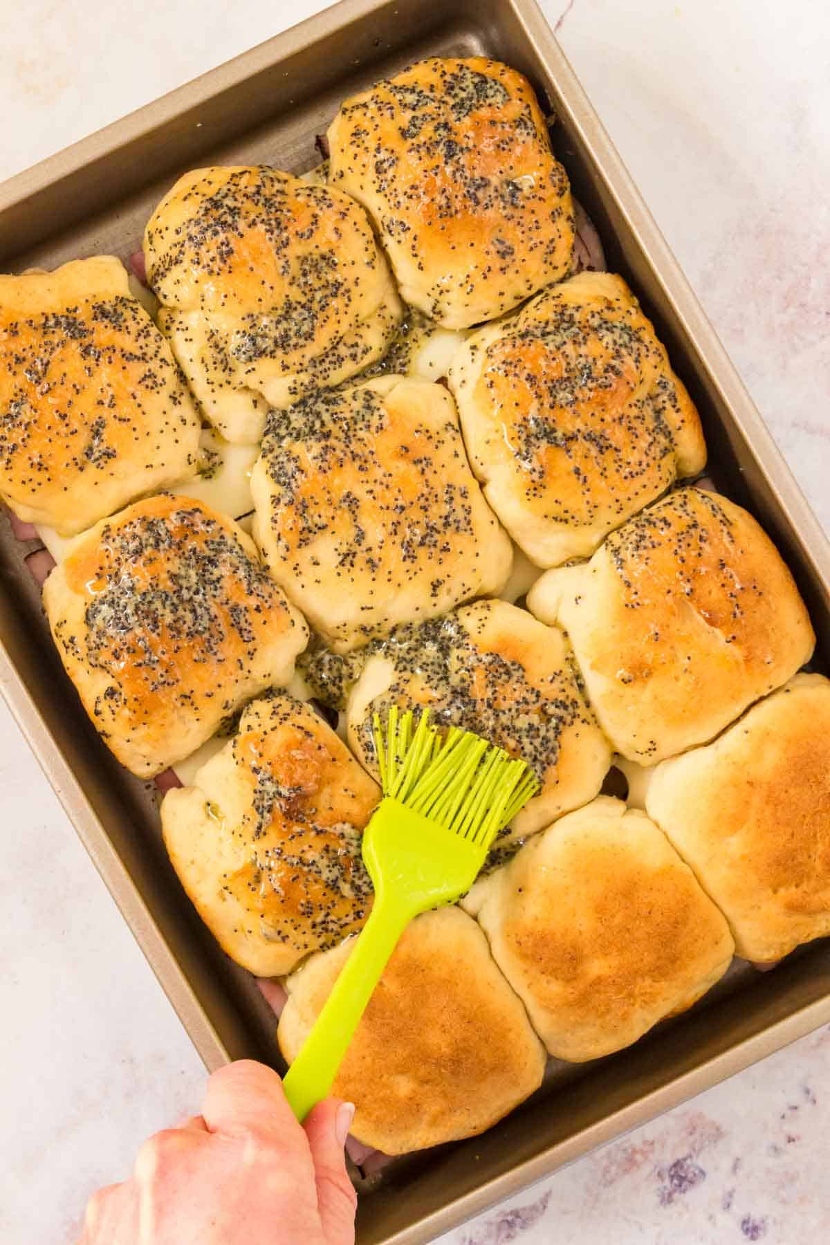 A pan of Hawaiian roll sliders is brushed with poppy seed glaze.
