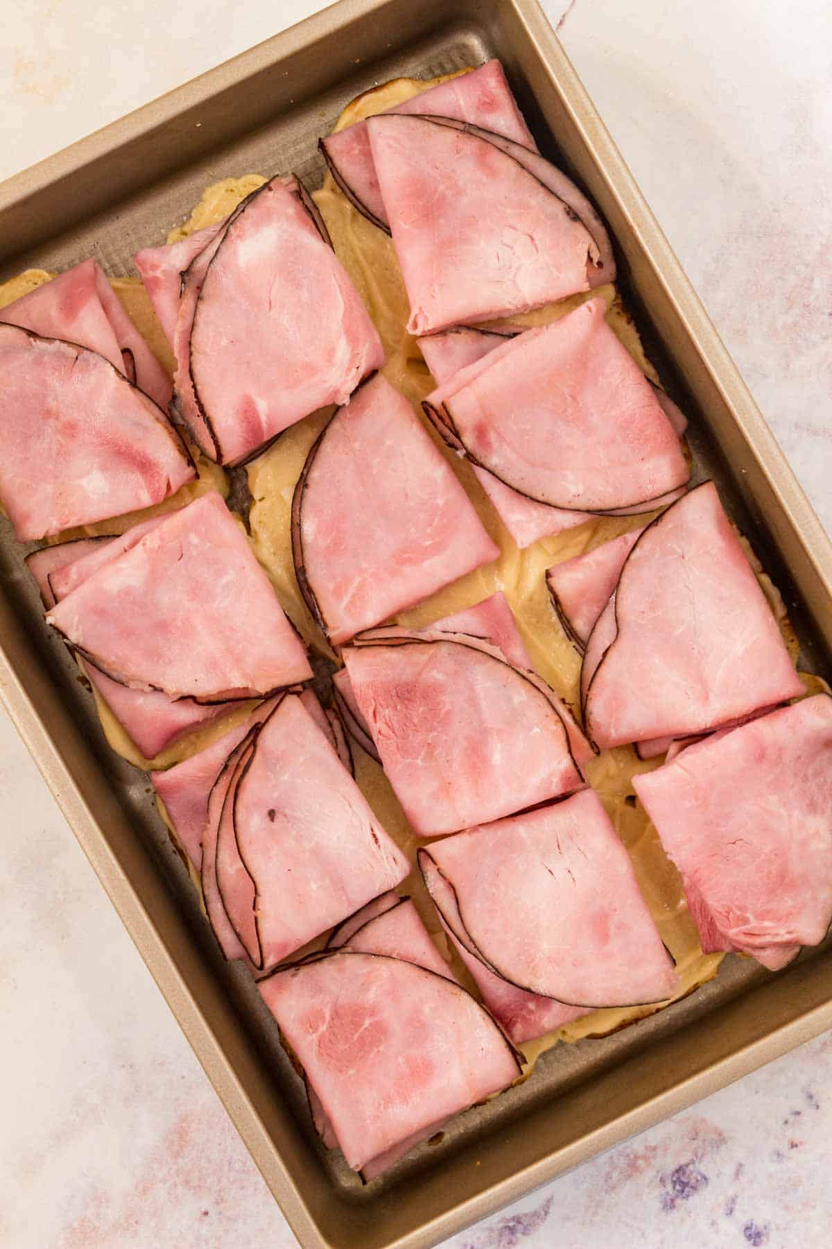 Slices of ham added to a pan full of Hawaiian rolls.